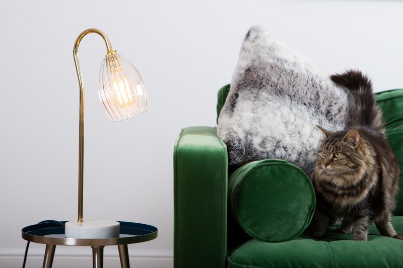 Ribbed table lamp featuring gold stand and marble based. Styled on a side table with green velvet sofa.