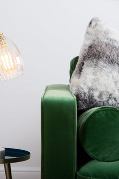 Ribbed table lamp featuring gold stand and marble based. Styled on a side table with green velvet sofa.