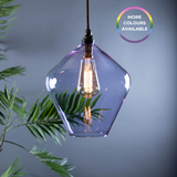 Decorative coloured pendant light with a geometric glass shade and visible antique style bulb, against a dark neutral background.