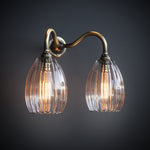 Double armed wall light featuring brass arm and medium sized ribbed shades. Lights are illuminated by two large antique bulbs