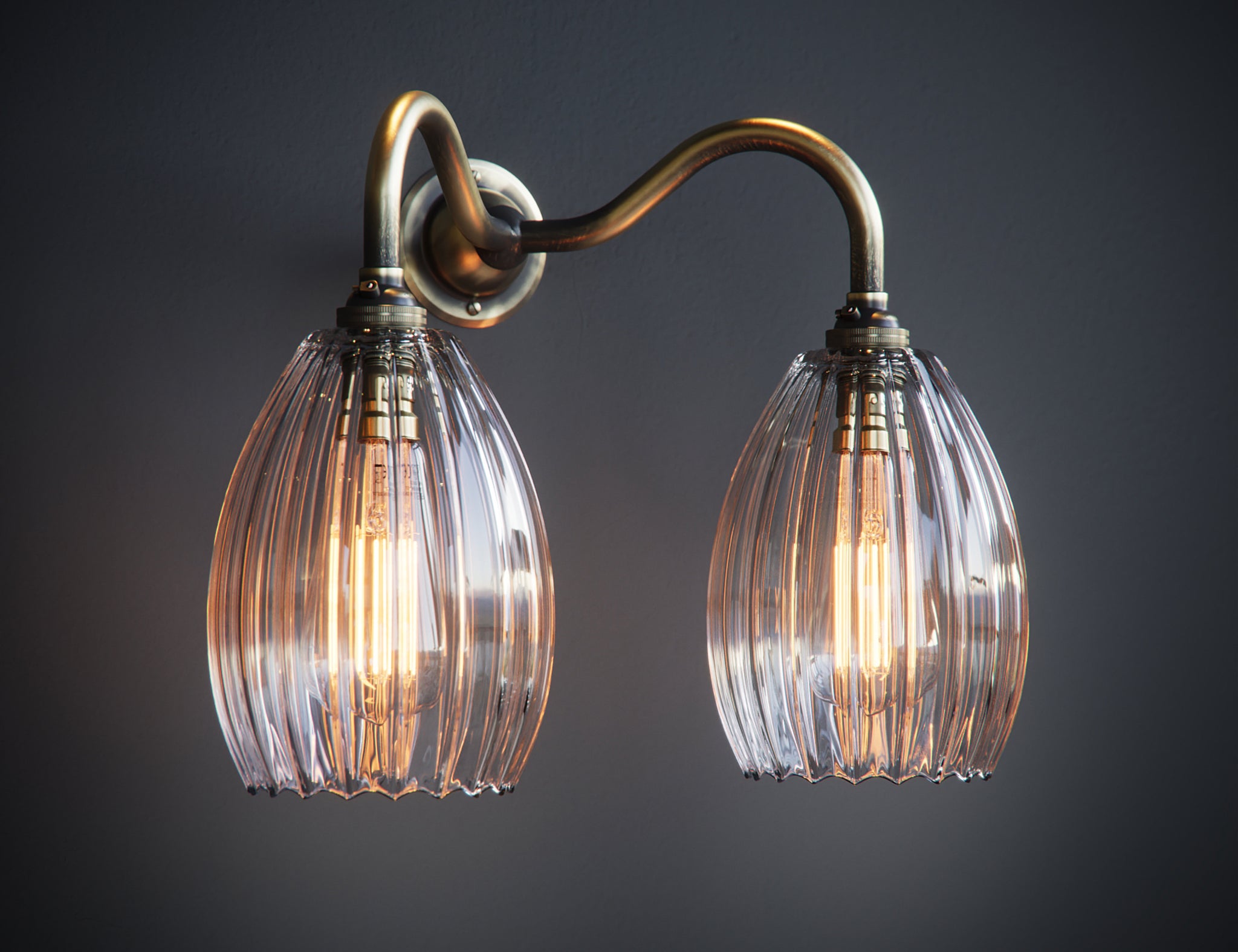 Double armed wall light featuring brass arm and medium sized ribbed shades. Lights are illuminated by two large antique bulbs