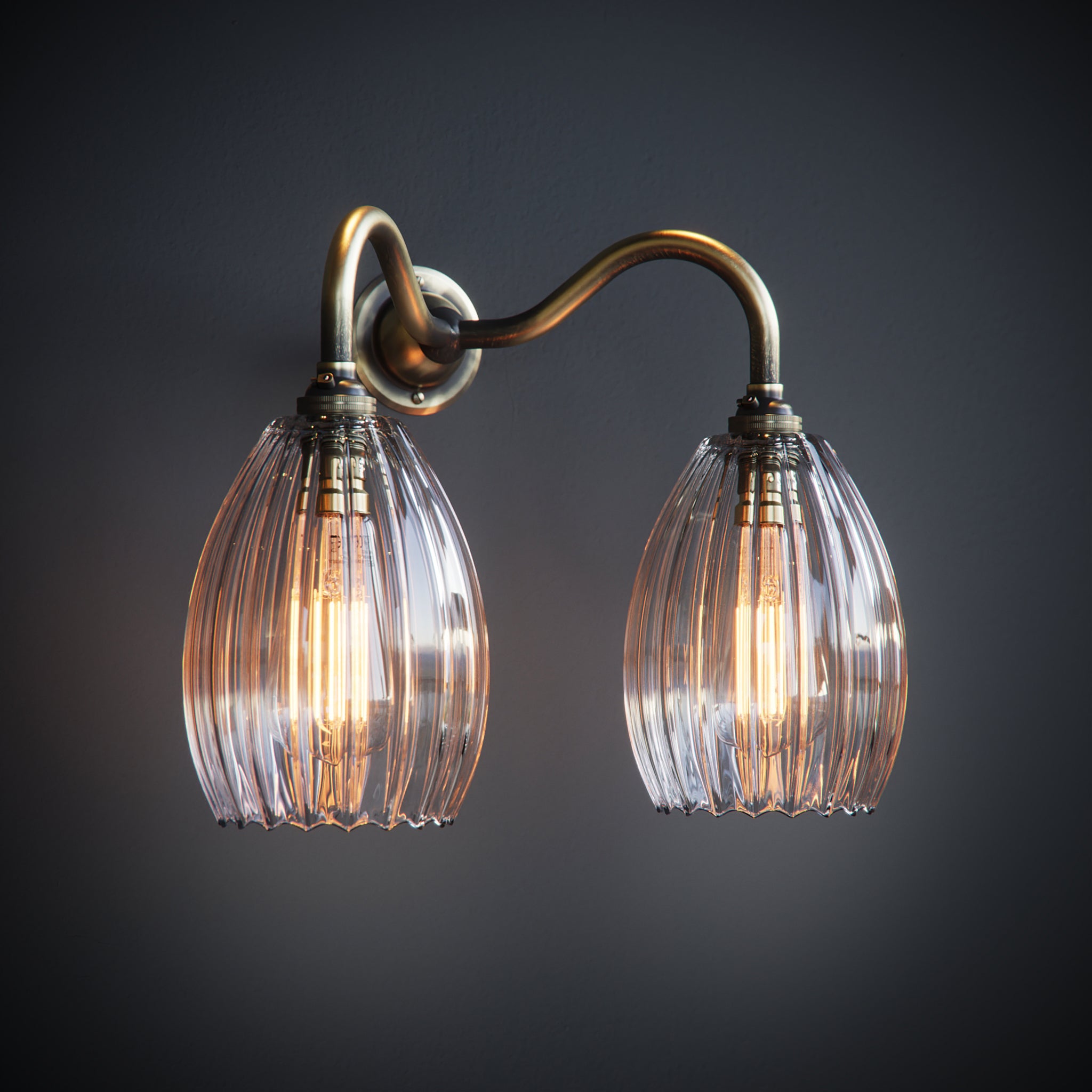 Double armed wall light featuring brass arm and medium sized ribbed shades. Lights are illuminated by two large antique bulbs