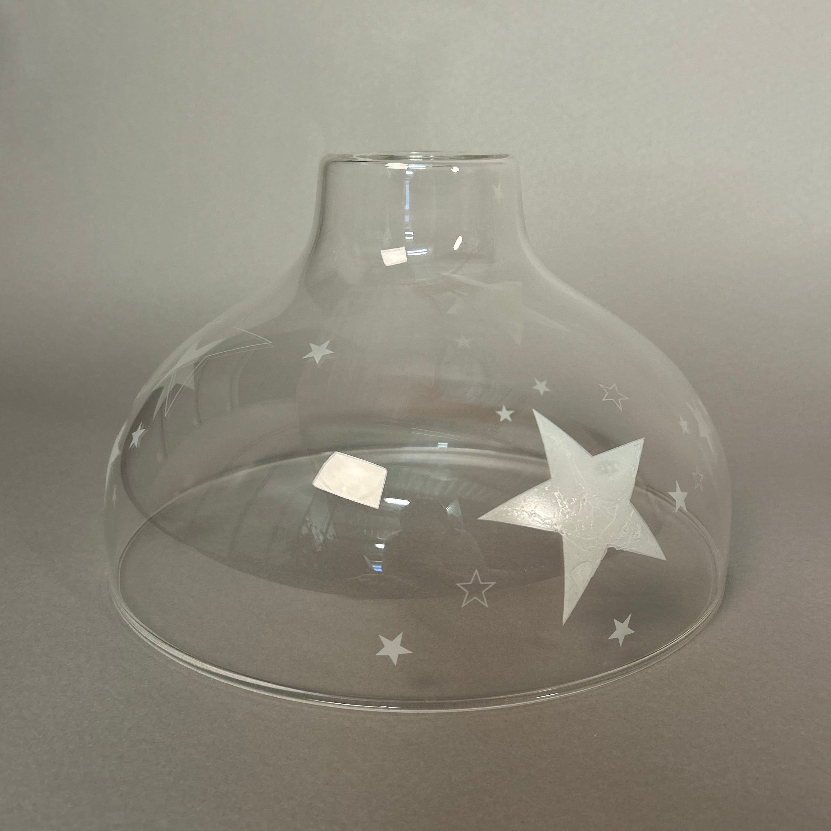 Clear glass pendant light with star designs on a grey background