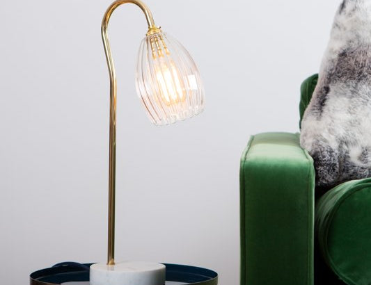 Ribbed table lamp featuring gold stand and marble based. Styled on a side table with green velvet sofa.