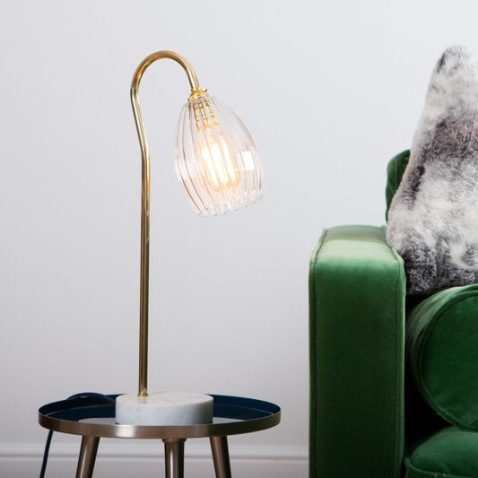 Ribbed table lamp featuring gold stand and marble based. Styled on a side table with green velvet sofa.