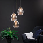 Illuminated Trio of Ribbed Glass Pendants style with a plant and armchair. 