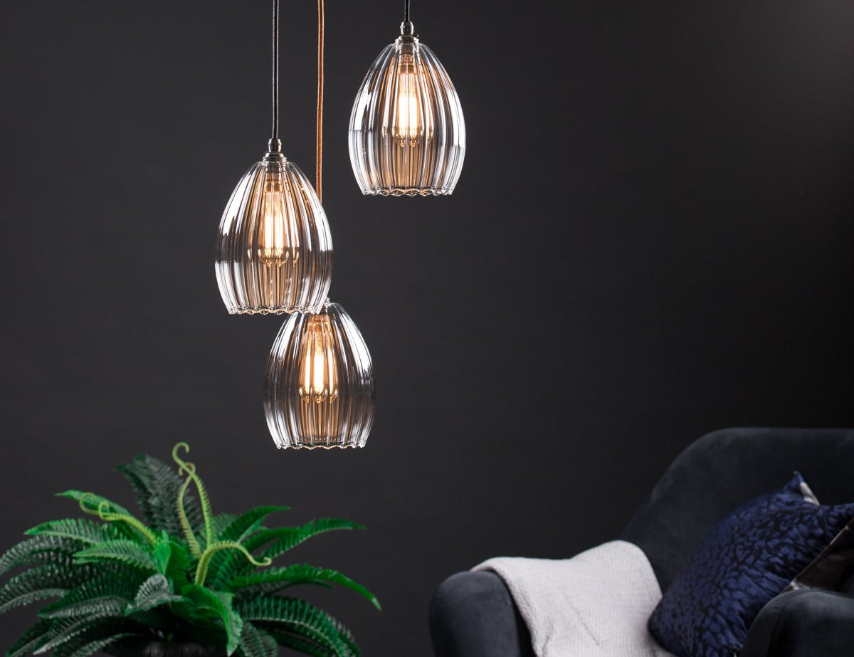 Illuminated Trio of Ribbed Glass Pendants style with a plant and armchair. 