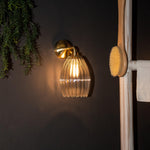 Illuminated glass pendant wall light in bathroom setting with brass wall plate