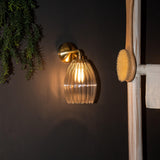 Illuminated glass pendant wall light in bathroom setting with brass wall plate
