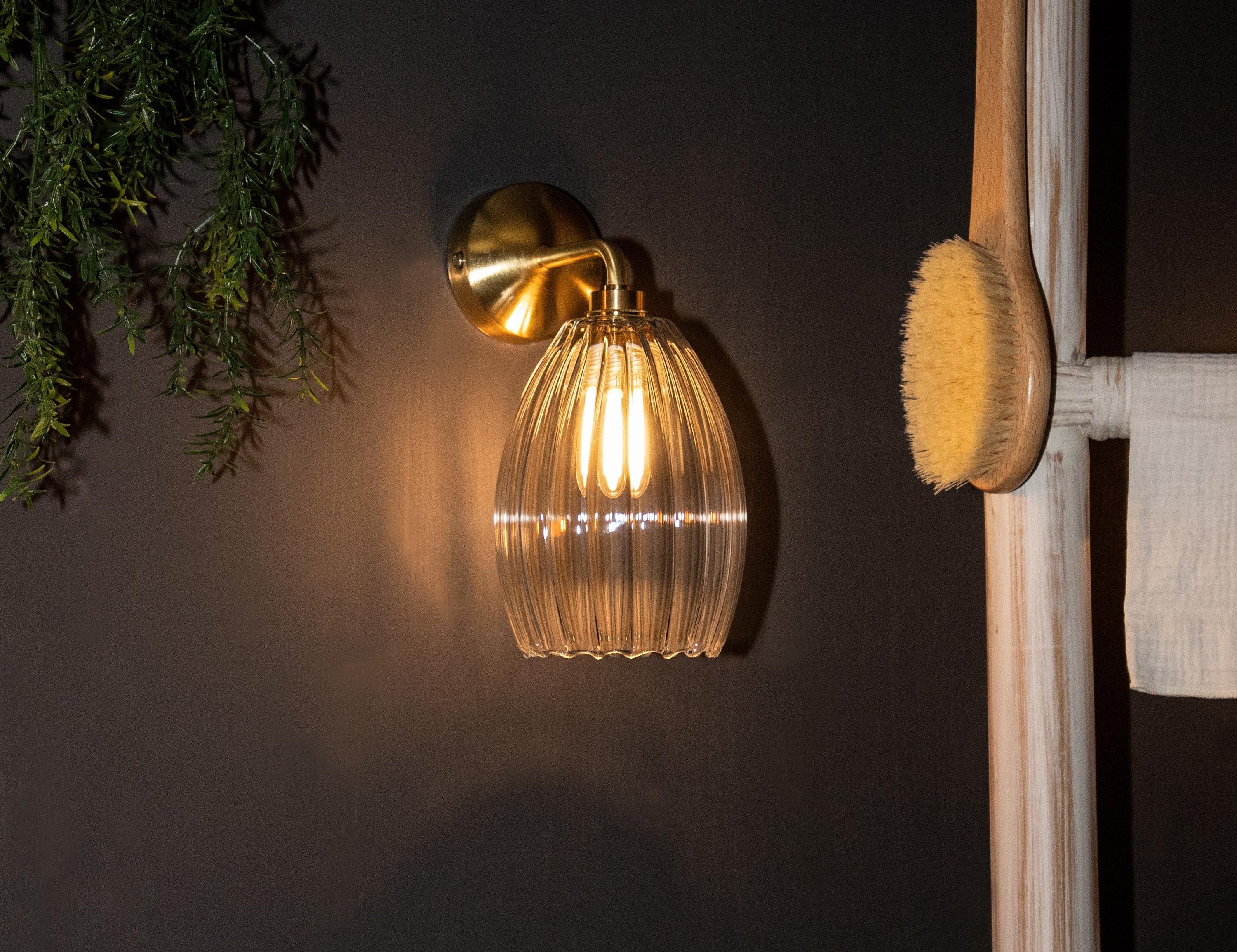 Illuminated glass pendant wall light in bathroom setting with brass wall plate